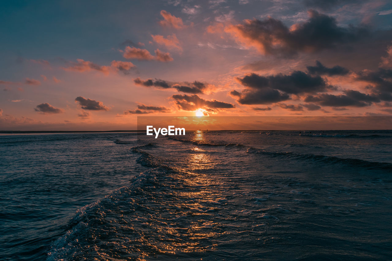 Scenic view of sea against cloudy sky during sunset