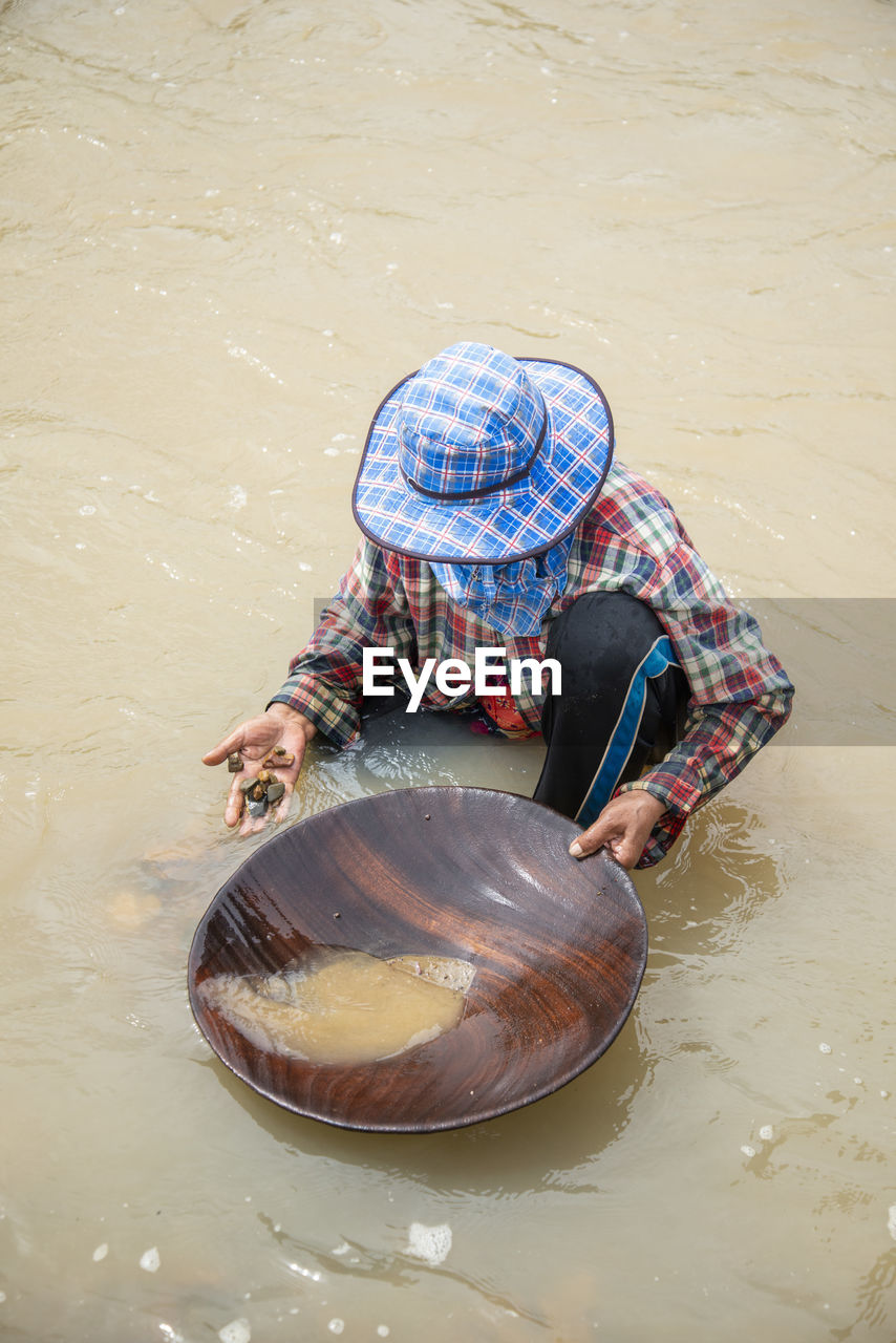 water, one person, hat, adult, men, high angle view, occupation, nature, clothing, container, outdoors, lifestyles, sitting, day, women, traditional clothing, full length, casual clothing, asian style conical hat, person, working, cleaning, river, tradition