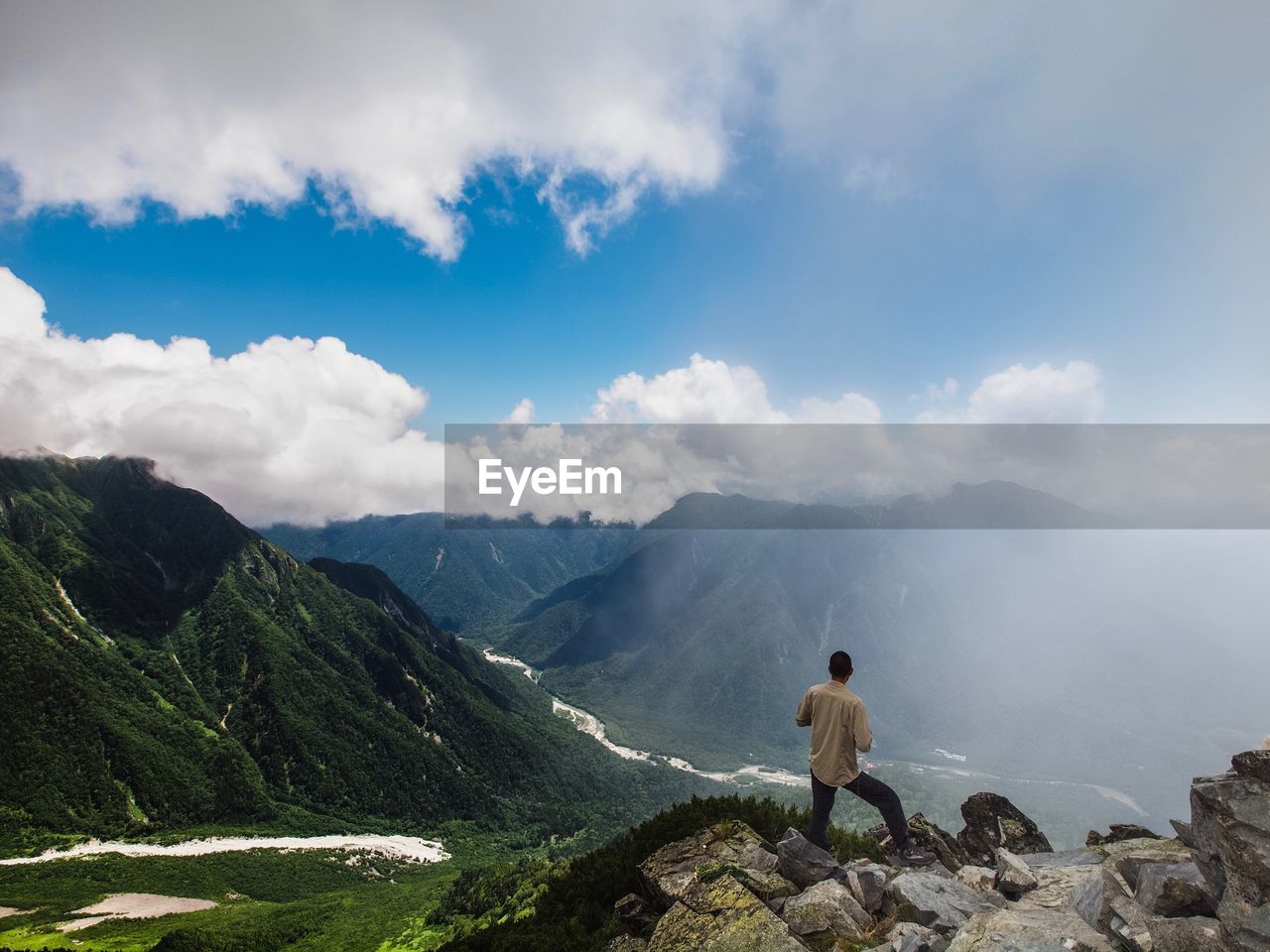 MAN STANDING ON ROCKS AGAINST MOUNTAIN RANGE