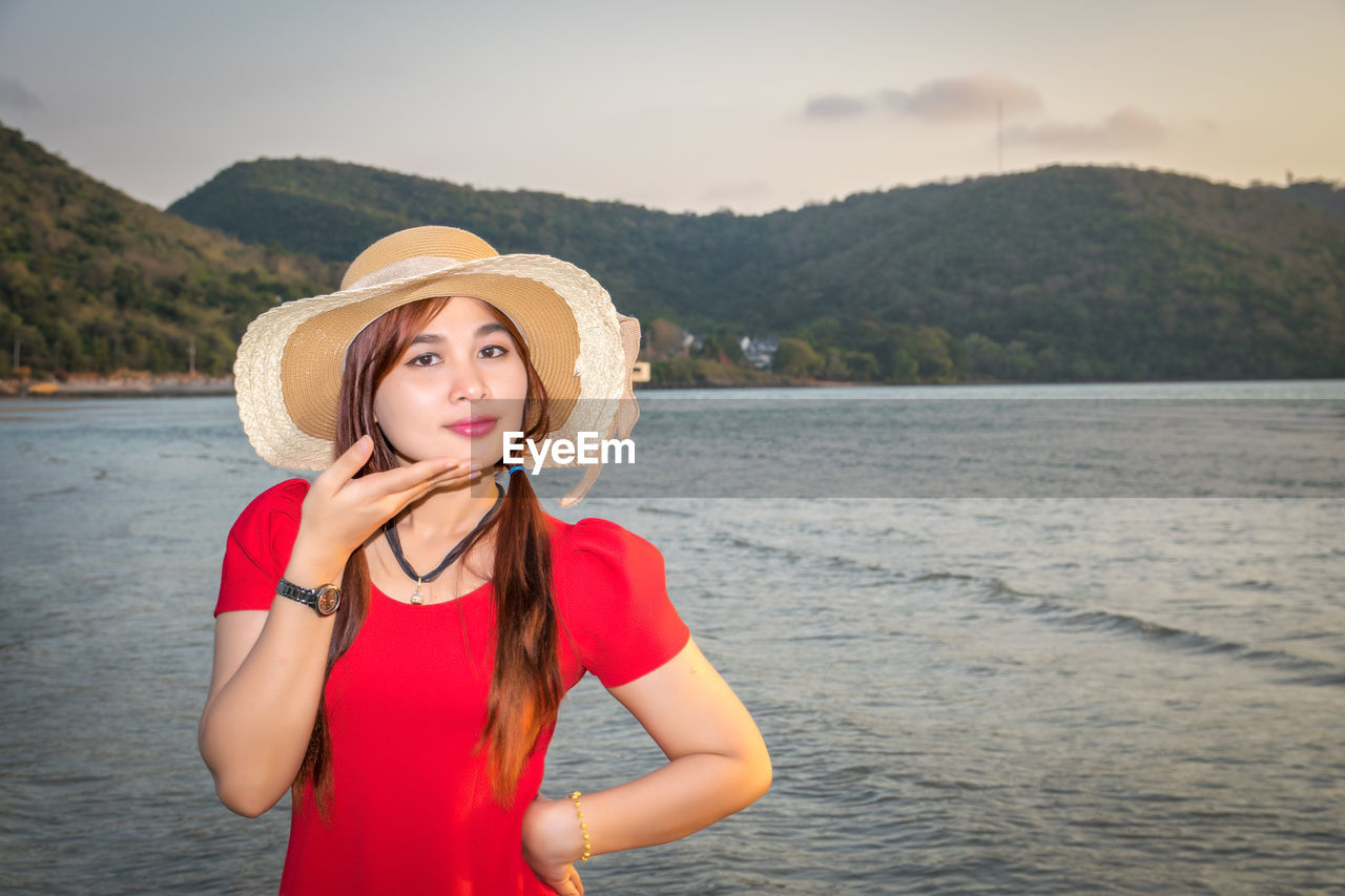 Portrait of beautiful woman with hand on chin standing on beach