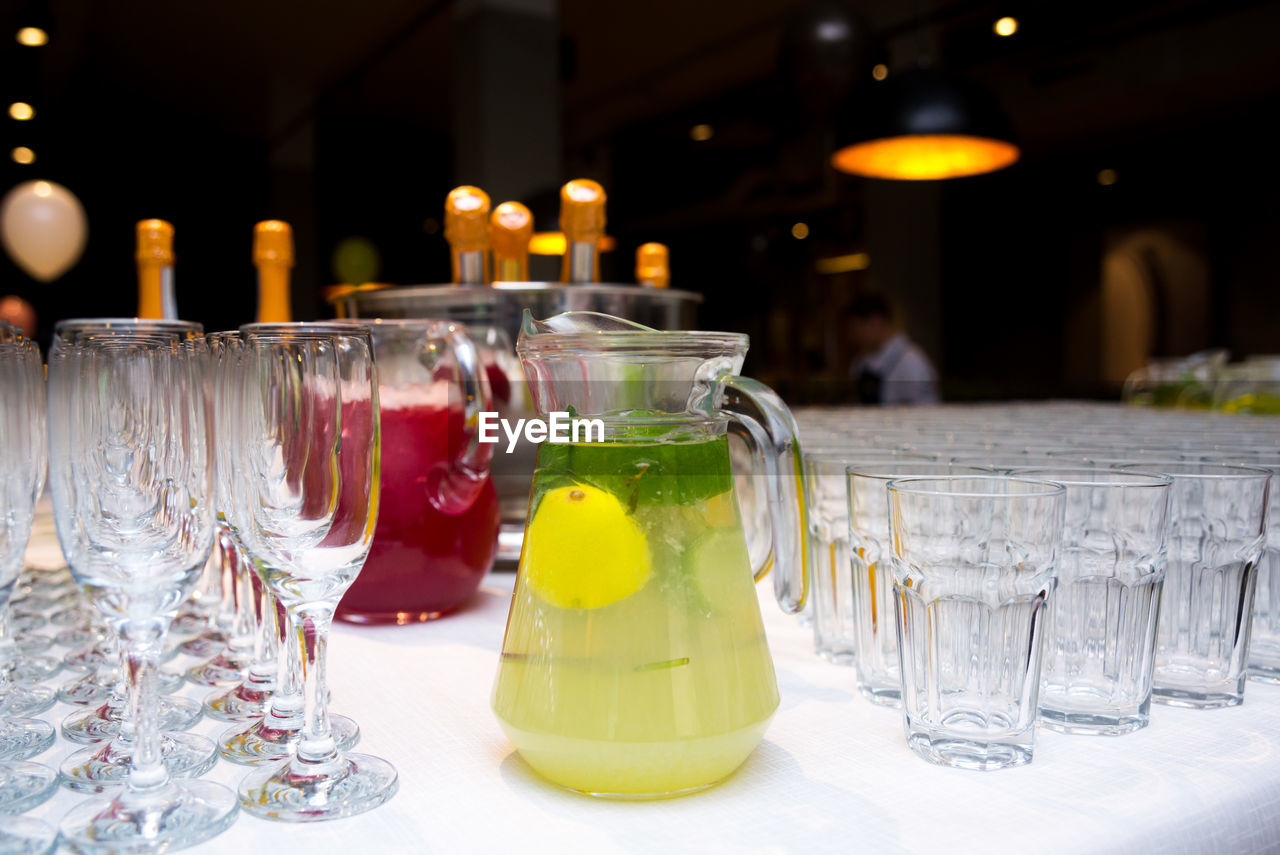 Soft drinks lemonades in large glass jugs on the table surrounded with empty glasses