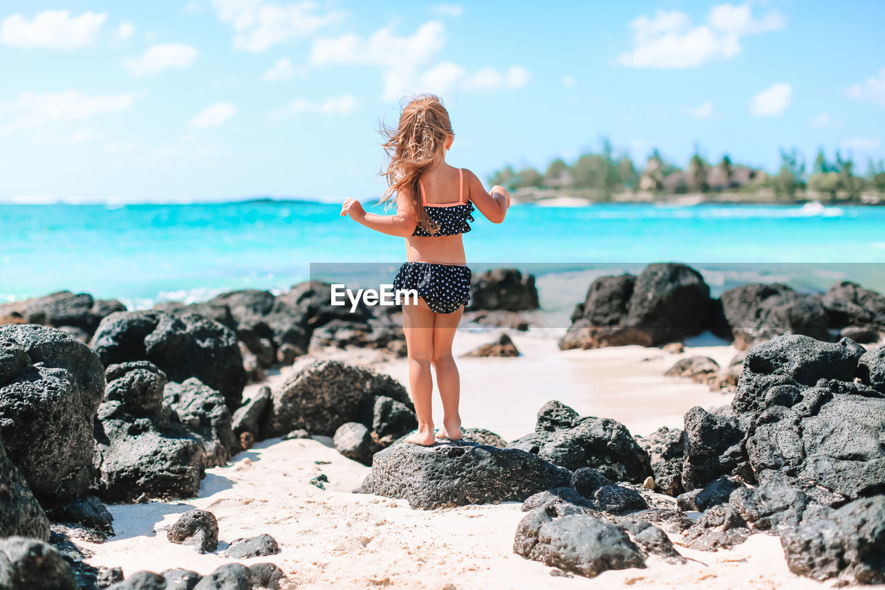 FULL LENGTH OF YOUNG WOMAN STANDING ON ROCK AT BEACH