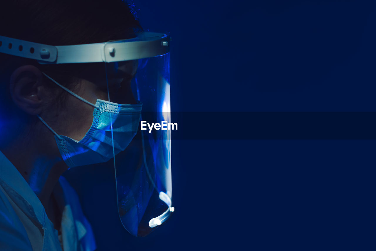 Close-up of doctor wearing face shield against blue background