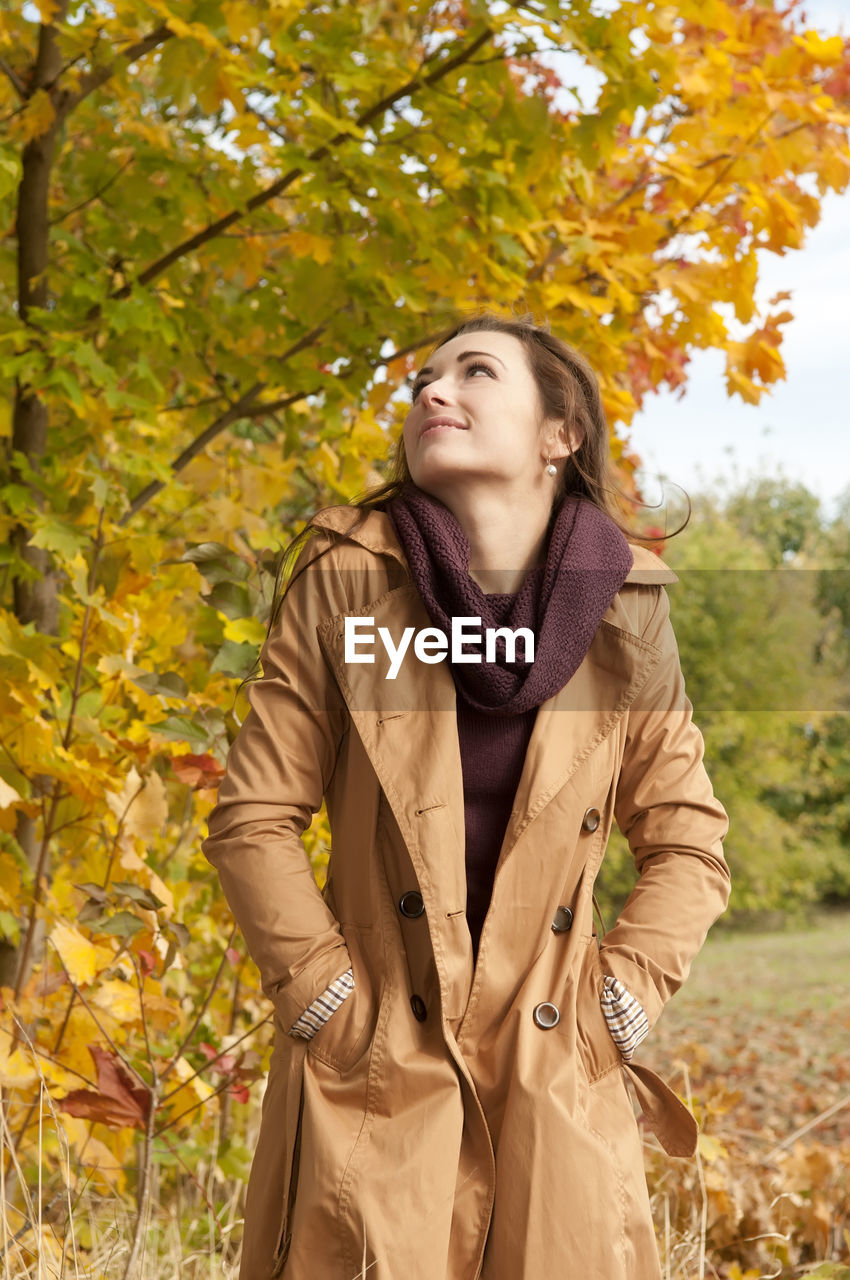 Woman wearing coat standing against trees in park during autumn