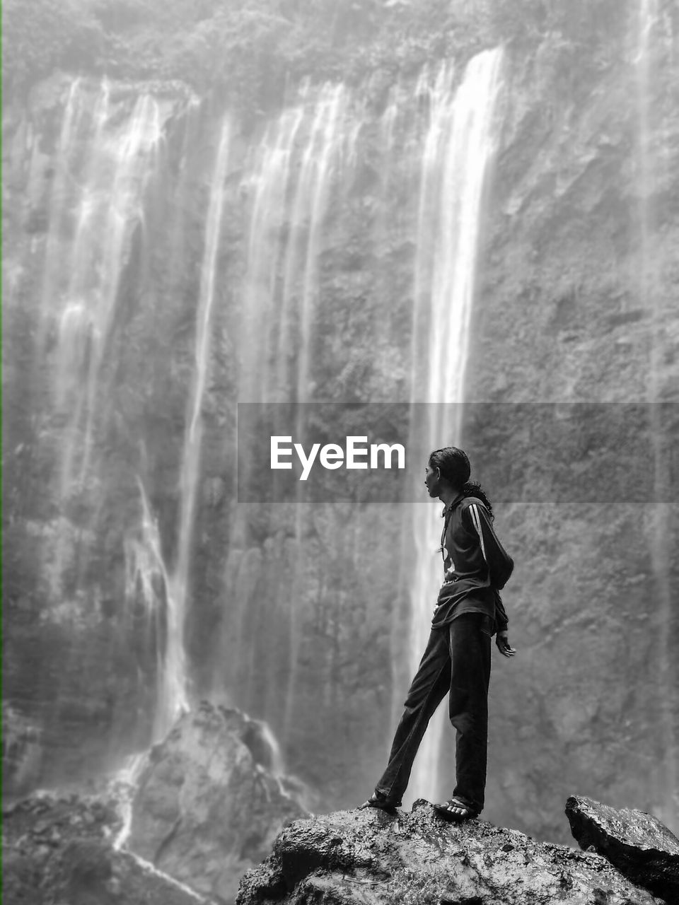 Side view of woman standing on rock against waterfall