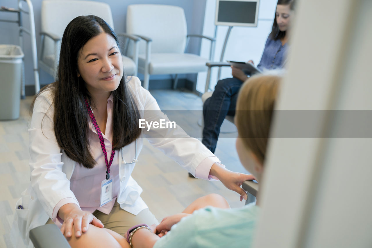 High angle view of pediatrician talking with patient while woman using tablet computer in background