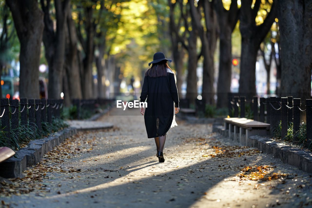 Rear view of woman walking on footpath during autumn