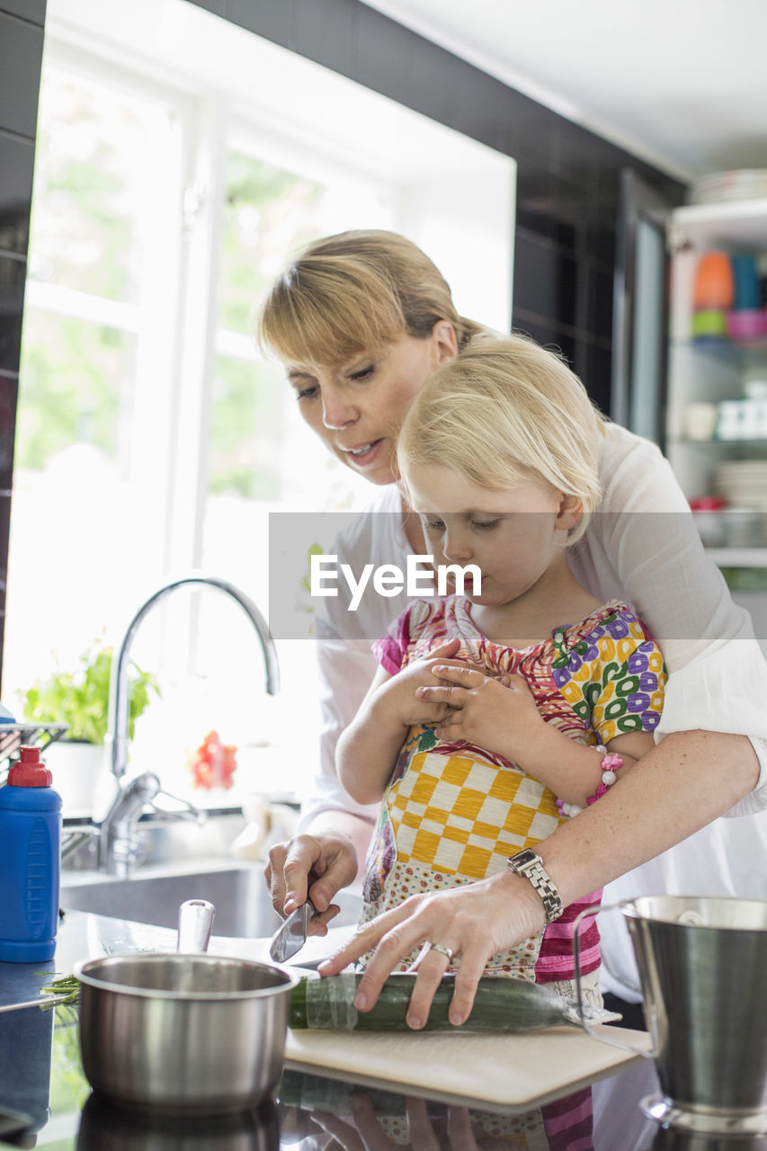 Mother teaching daughter to cut vegetables in kitchen