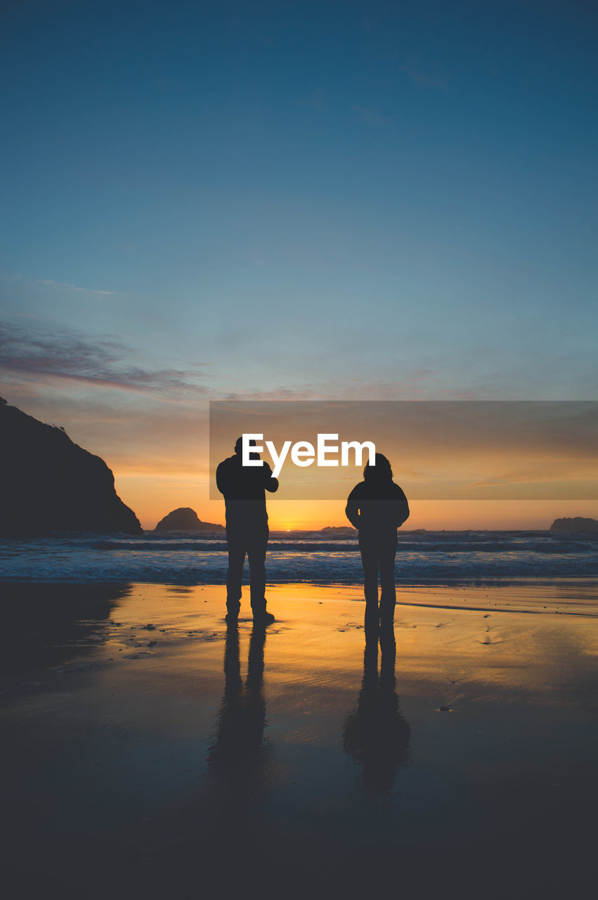 Silhouette of couple standing at beach during sunset