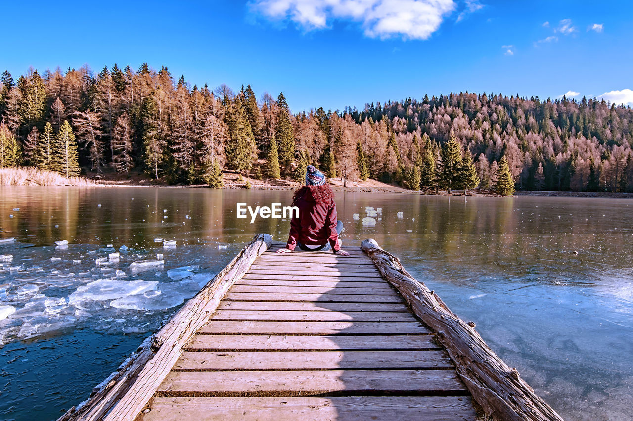 Rear view of woman sitting on pier over lake