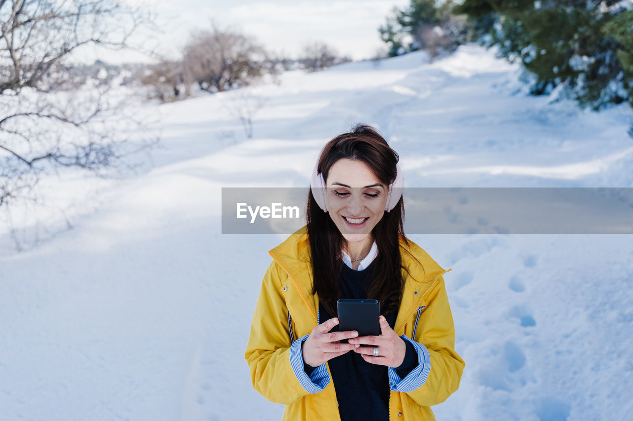 Young woman using phone while standing on snow