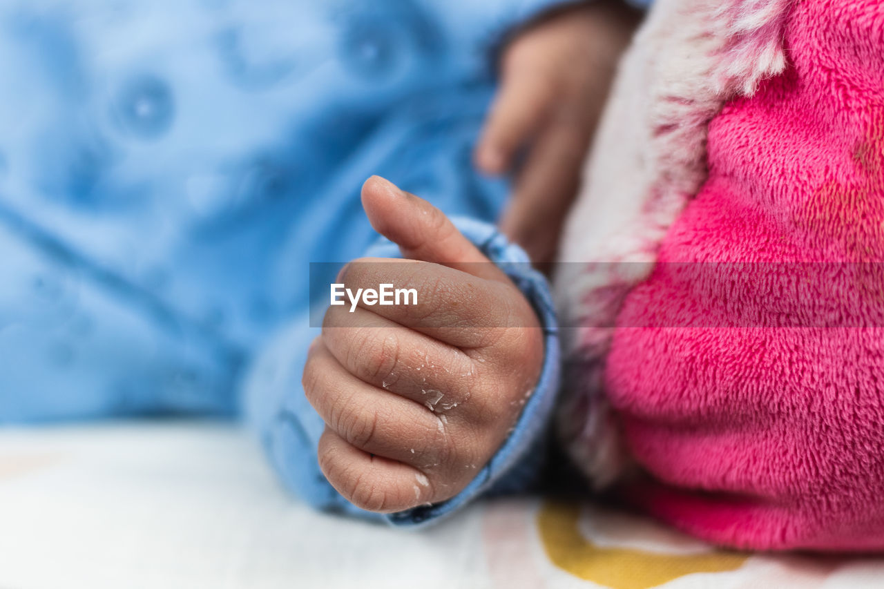 Cropped unrecognizable newborn baby lying on big toy on cozy blanket