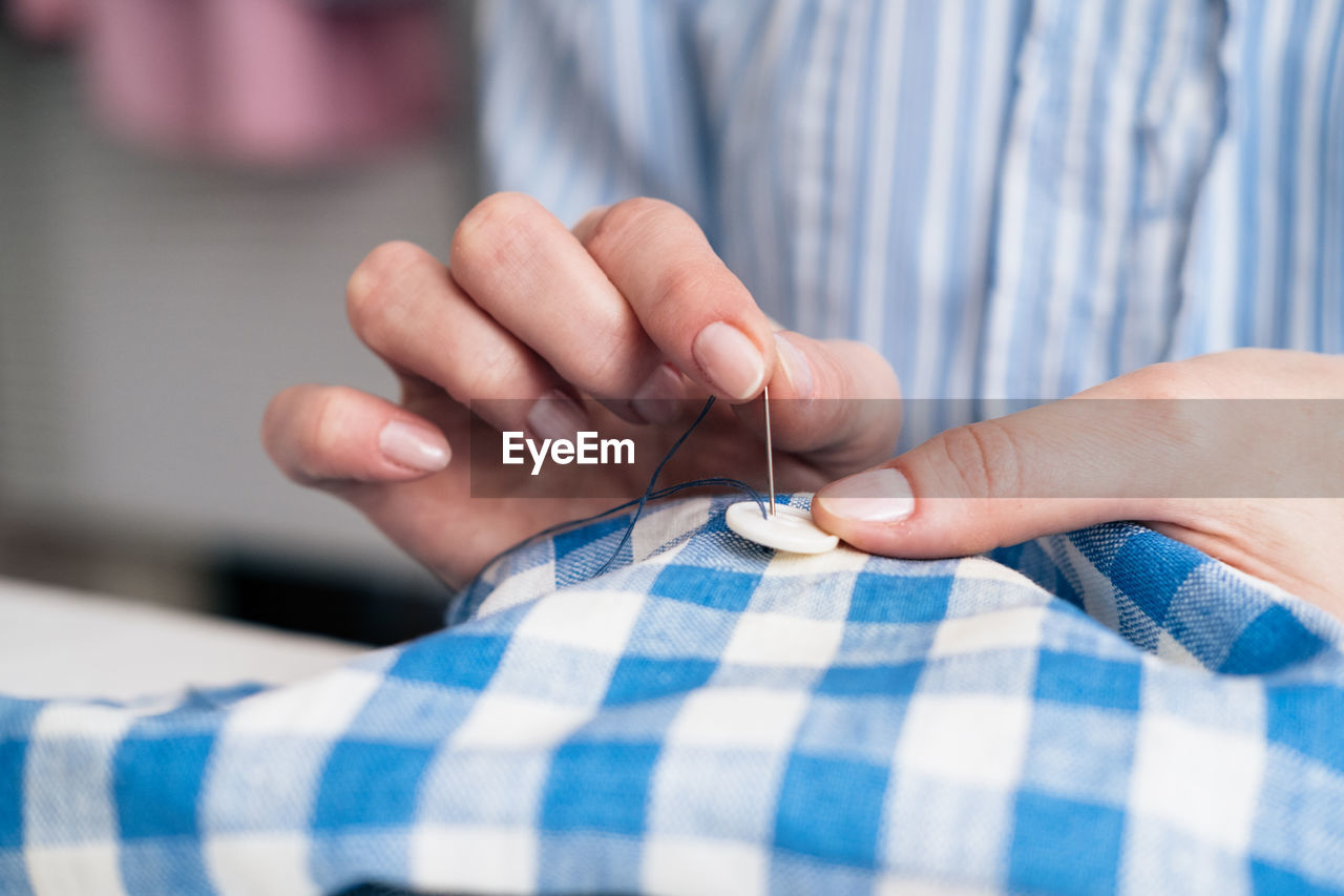 Midsection of craftswoman sewing button on textile at workshop