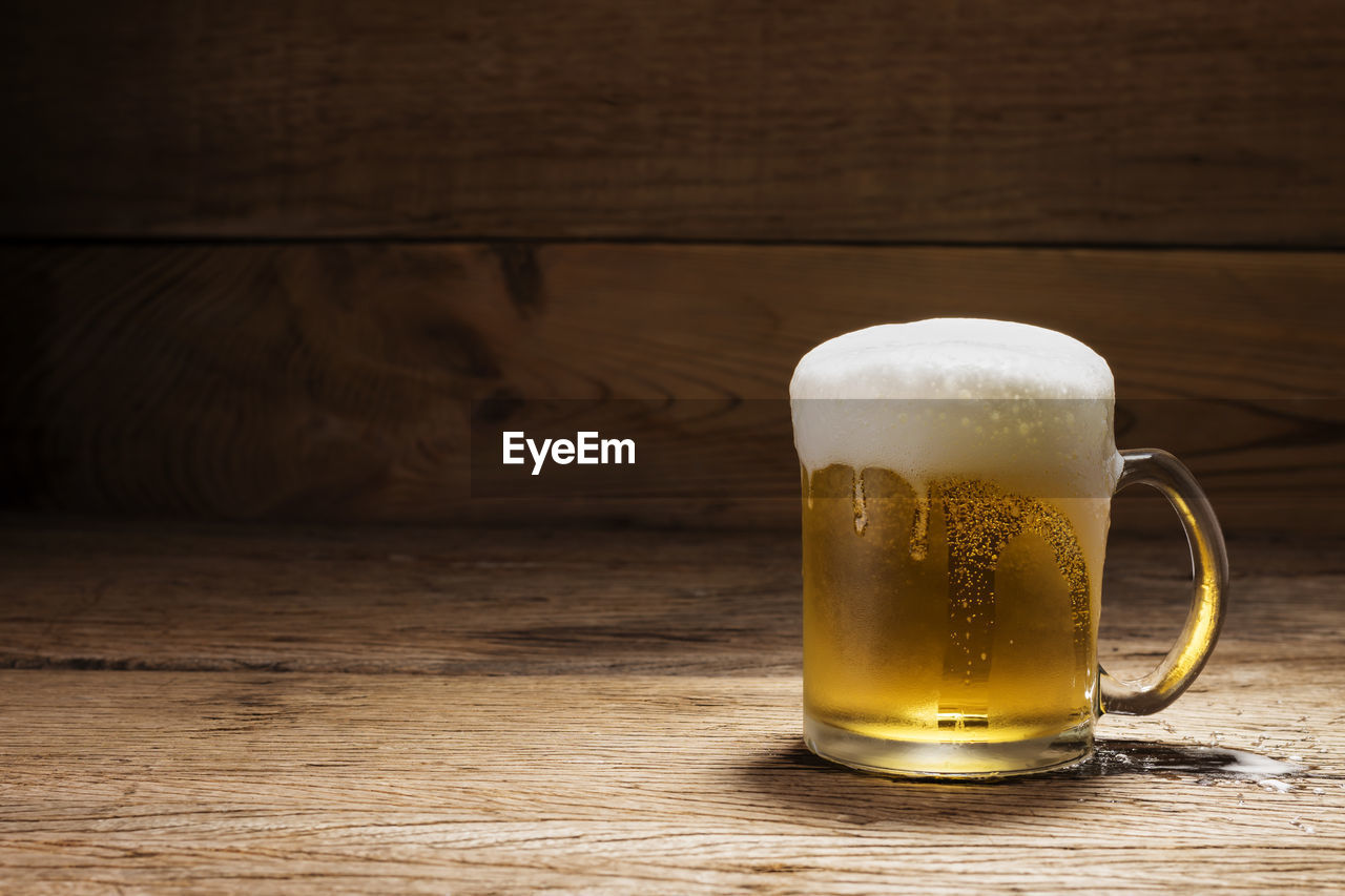 Beer glass with white beer foam on a dark wooden table background