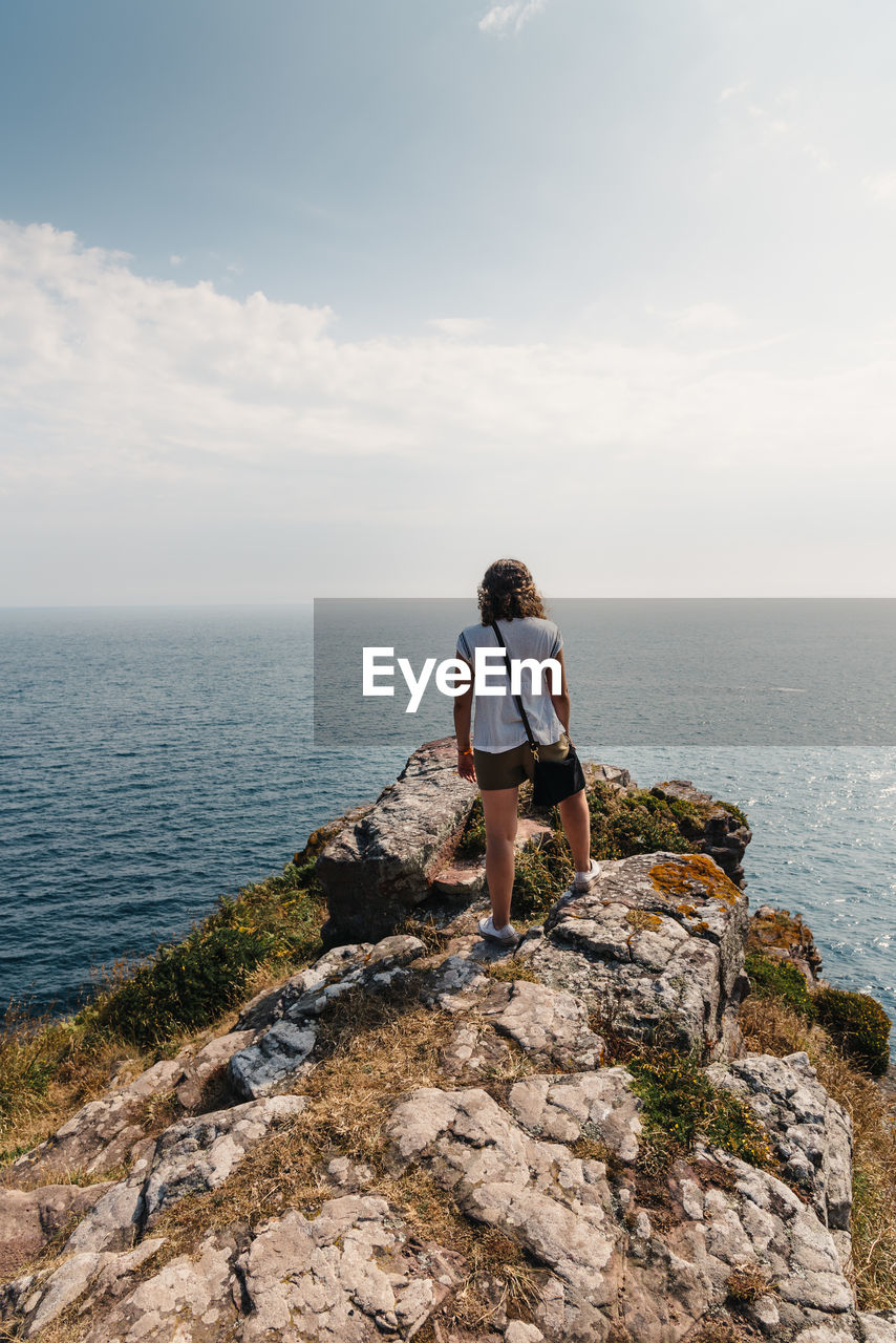 Rear view of woman standing on rock against sky