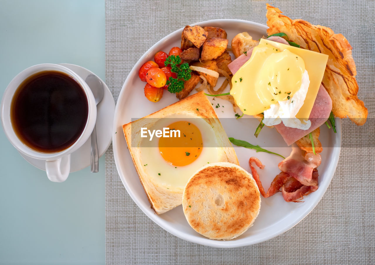 American breakfast with sunny side up eggs, bacon, toast, bread, croissant and coffee on table