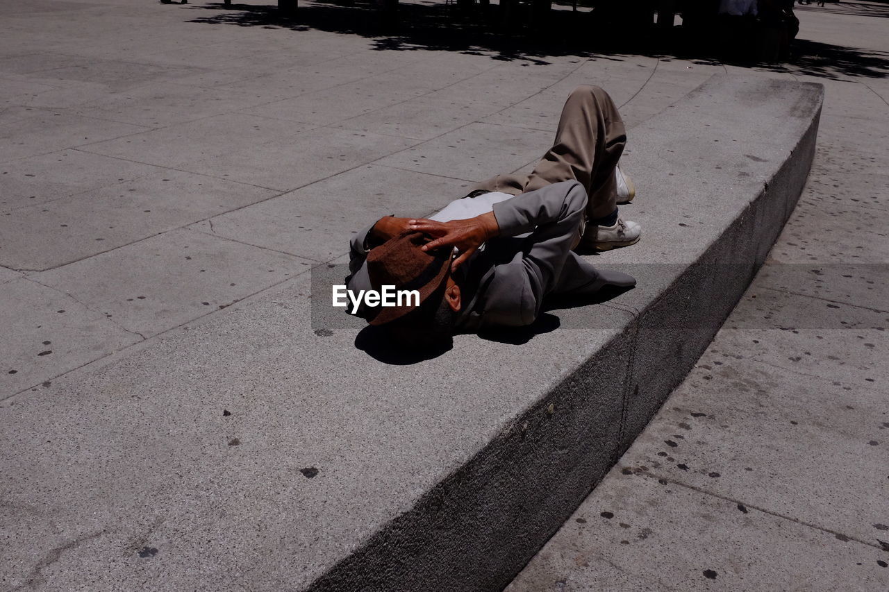 Homeless man sleeping on footpath with fedora hat on face