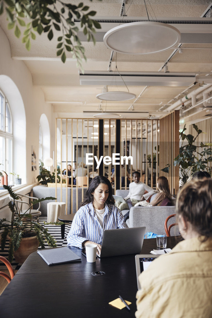 Businesswoman using laptop while working with colleagues at coworking office