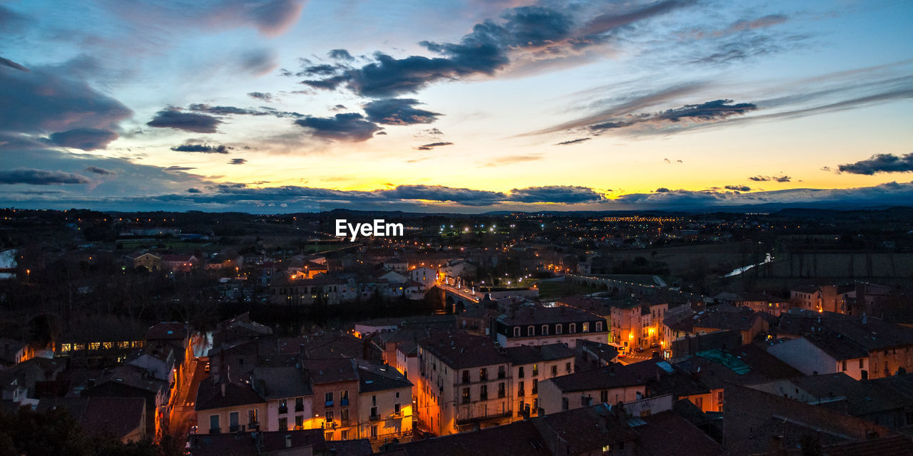 AERIAL VIEW OF ILLUMINATED CITY AGAINST SKY AT SUNSET