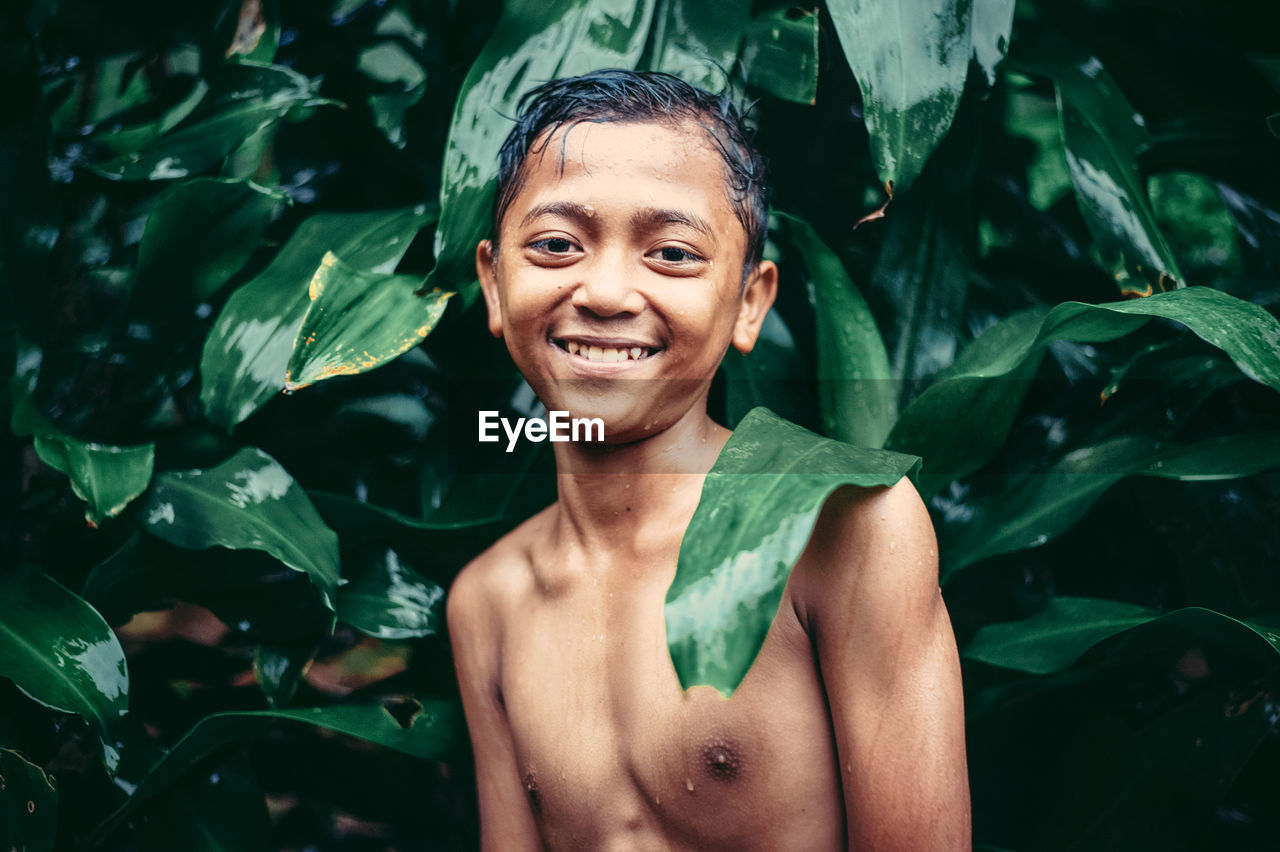 Portrait of smiling shirtless boy standing against plants