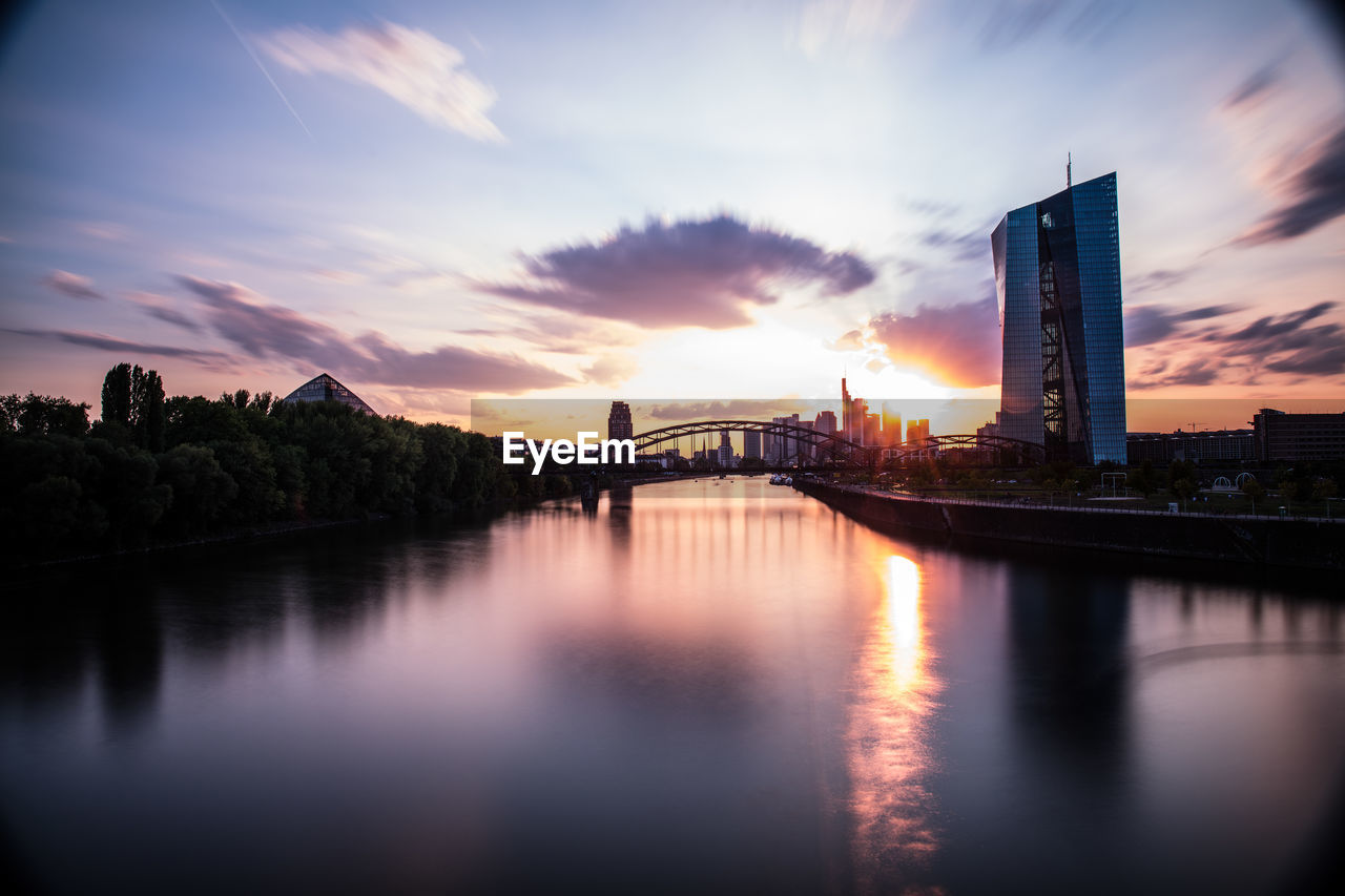 Scenic view of river by illuminated buildings against sky during sunset