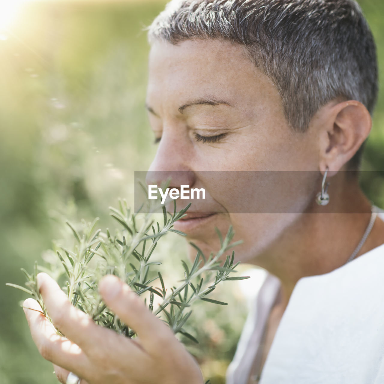 Woman with eyes closed holding while smelling rosemary plant