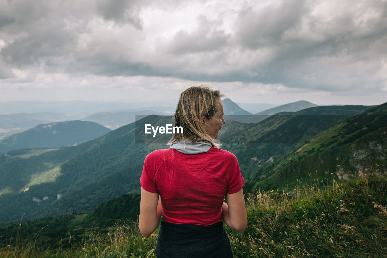 REAR VIEW OF WOMAN STANDING ON MOUNTAIN