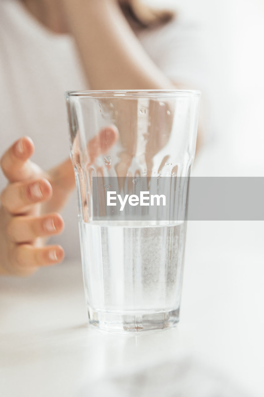 Close-up of a glass half filled with clean water. the child wants to take a glass and have a drink.