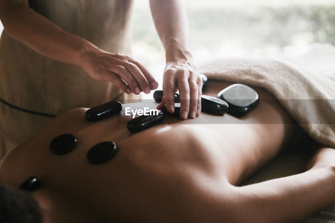 Midsection of masseuse giving lastone therapy to woman at spa