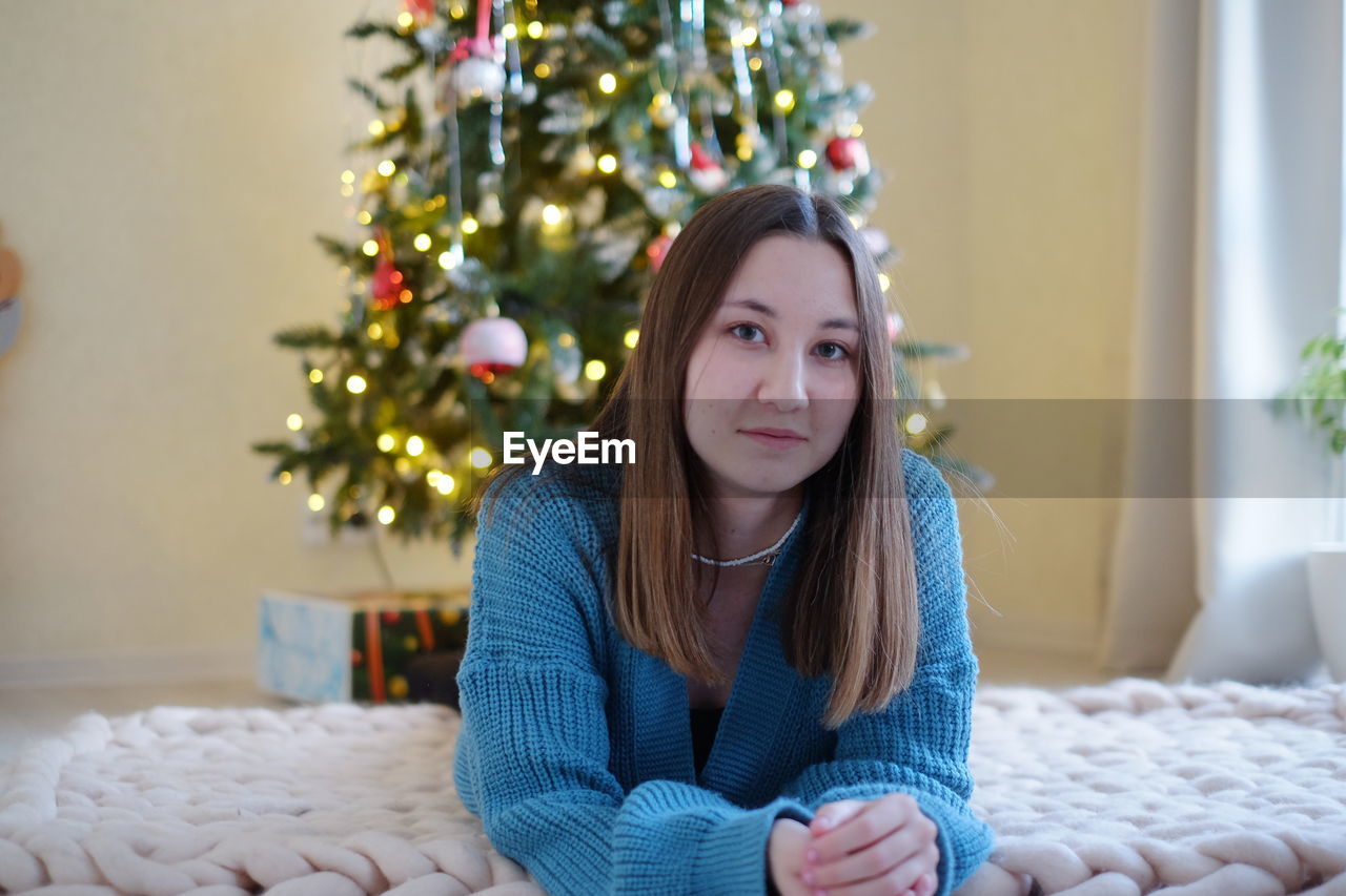 Portrait of young woman sitting near christmas tree
