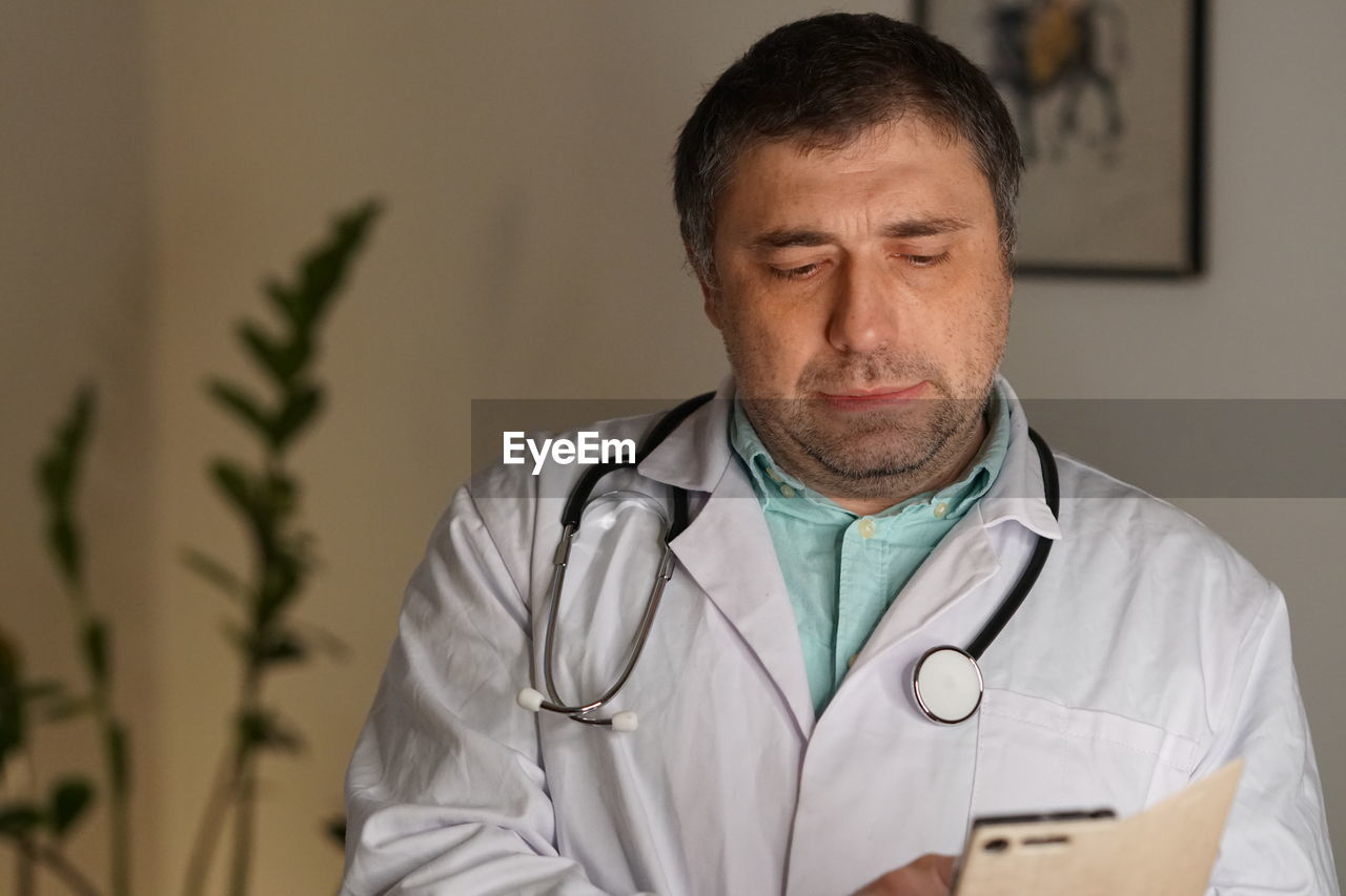 Close-up of mature doctor using phone against wall