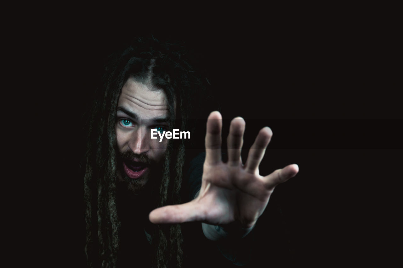 Close-up portrait of young man gesturing against black background