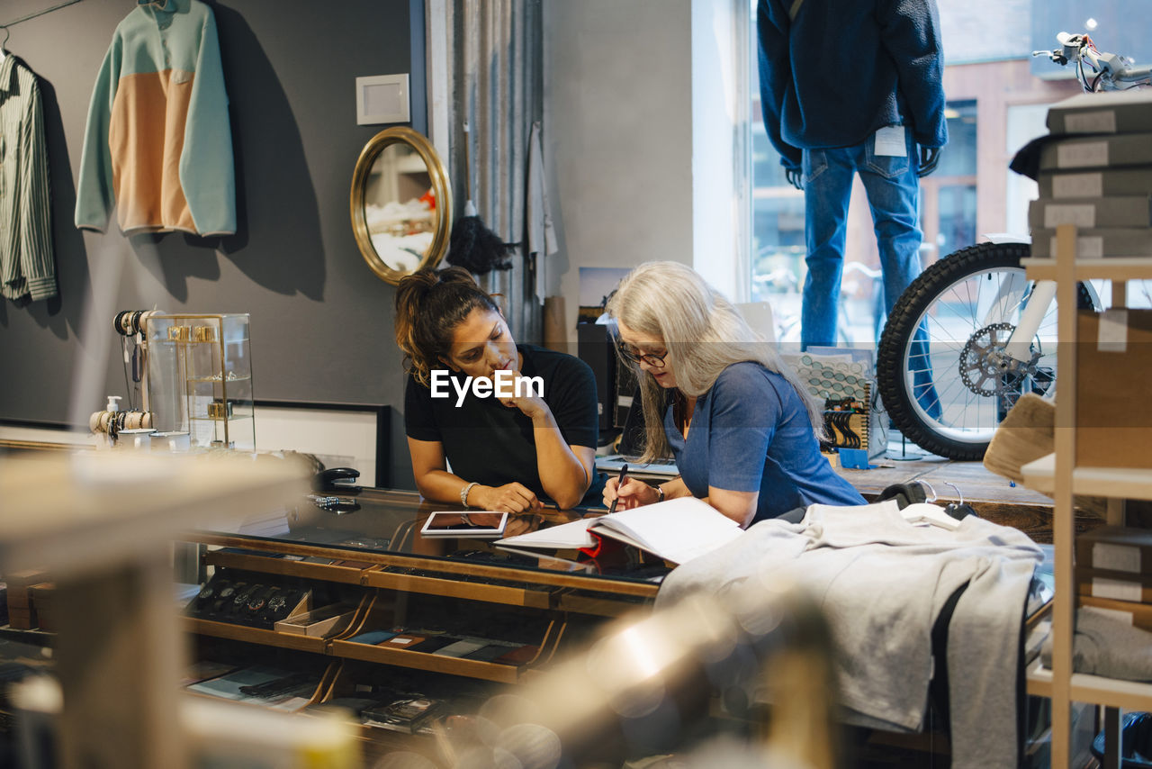 Female colleagues discussing over diary at retail store