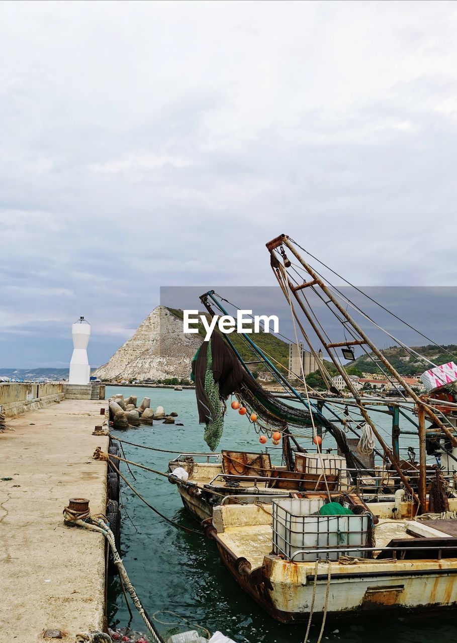 Fishing boats moored at harbor against sky