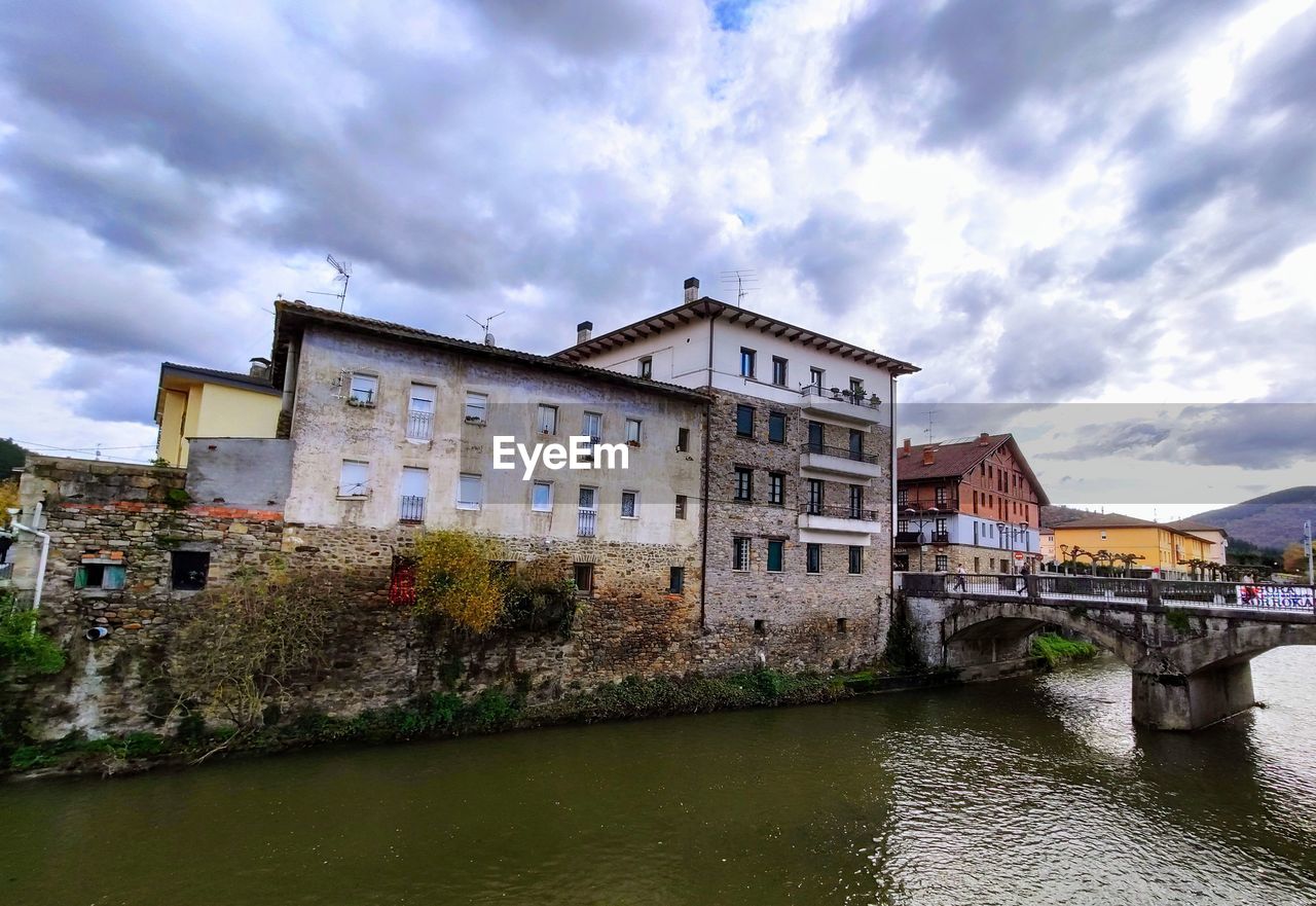 Bridge over river by buildings in city against sky