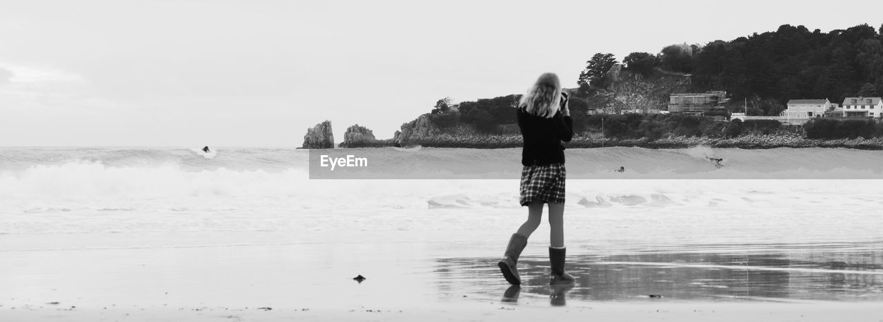 Rear view of woman walking at beach against sky