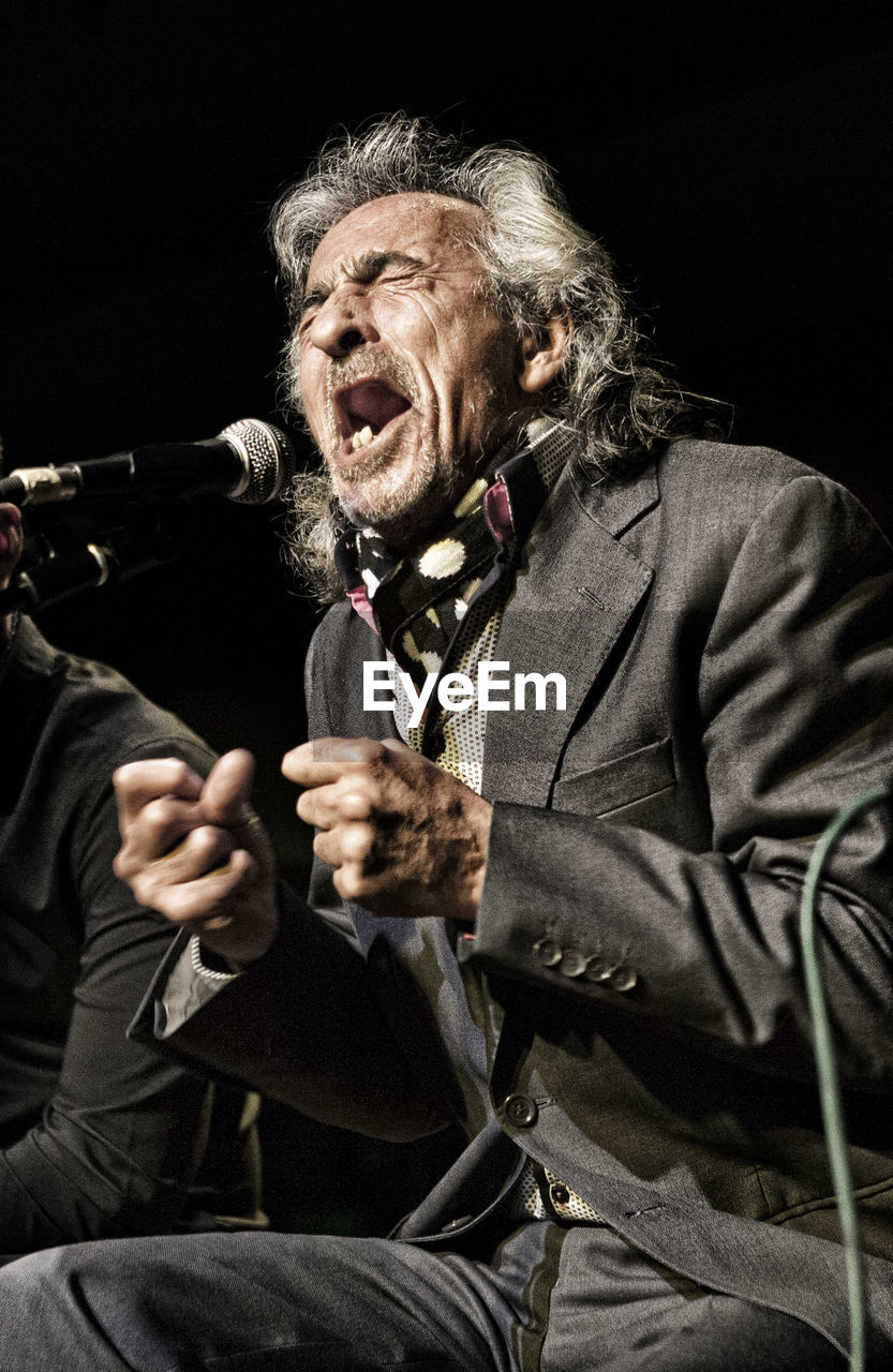 Senior man singing against black background