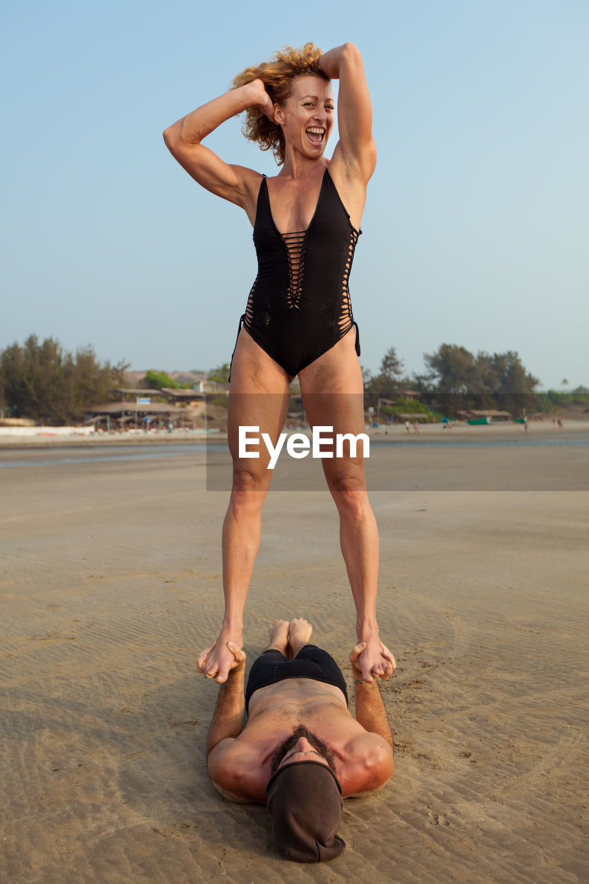 Happy woman standing on man at beach against sky