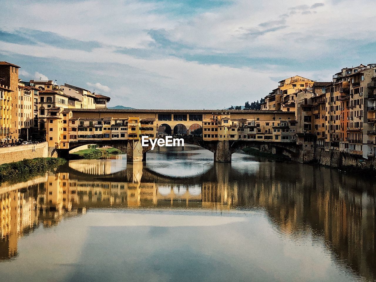 Arch bridge over river by buildings against sky