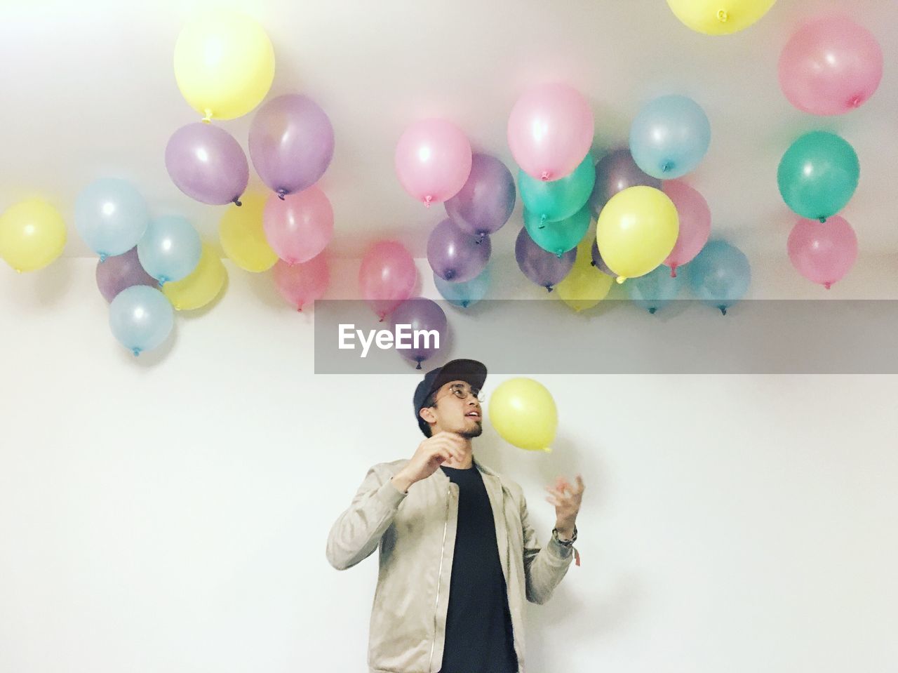 Young man with helium balloons standing under ceiling