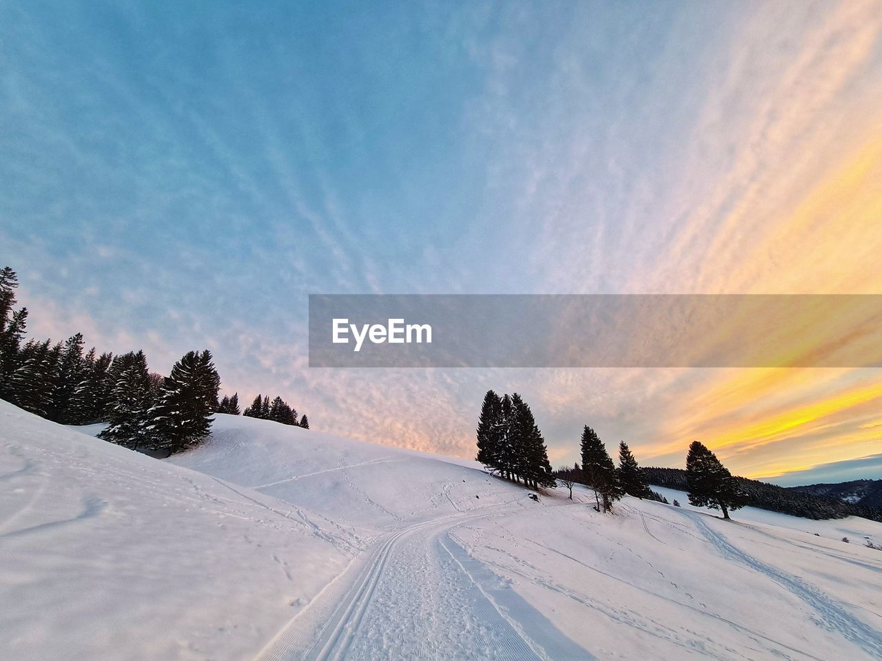 Snow covered field against sky during sunset