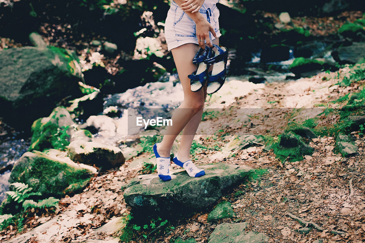 Young hipster girl staying on a rock at river in forest in printed bright socks