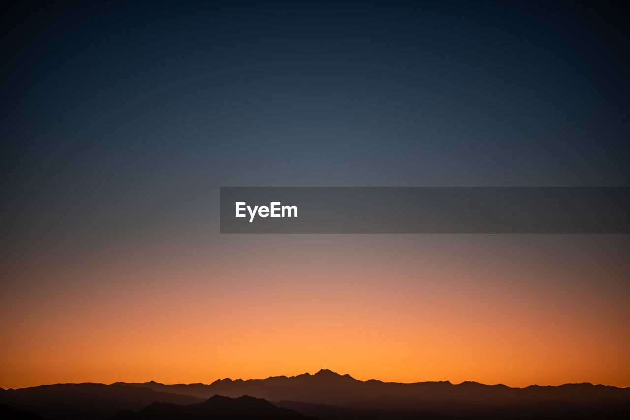 Scenic view of silhouette mountains against clear sky during sunset