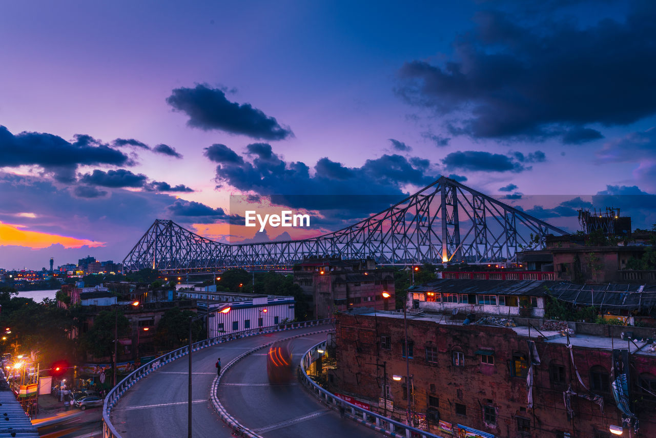 Bridge over illuminated city against sky at sunset
