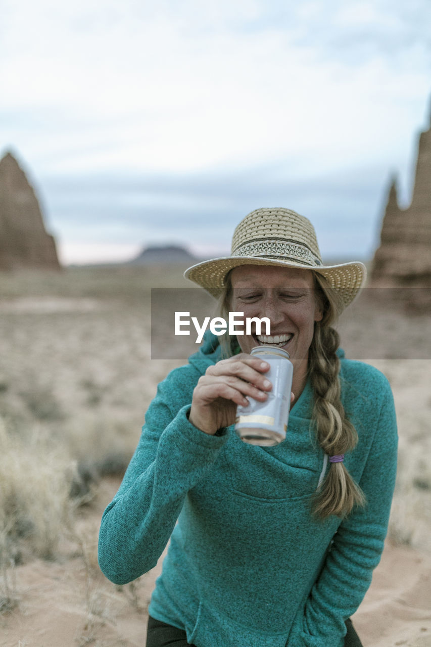 Cheerful female hiker wearing hat while having drink at desert