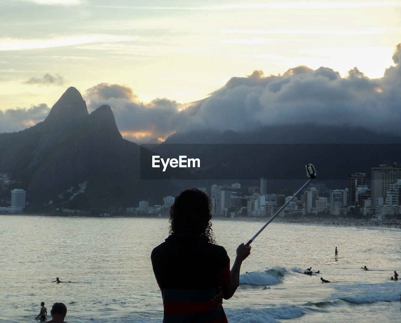 REAR VIEW OF MAN WITH WOMAN STANDING IN SEA AGAINST MOUNTAIN