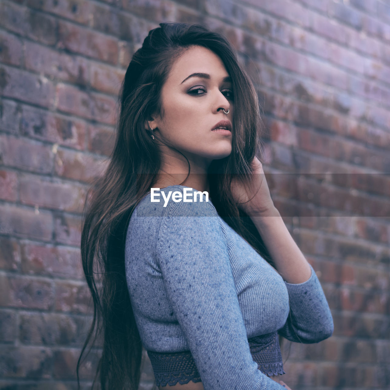 Portrait of young woman standing against brick wall