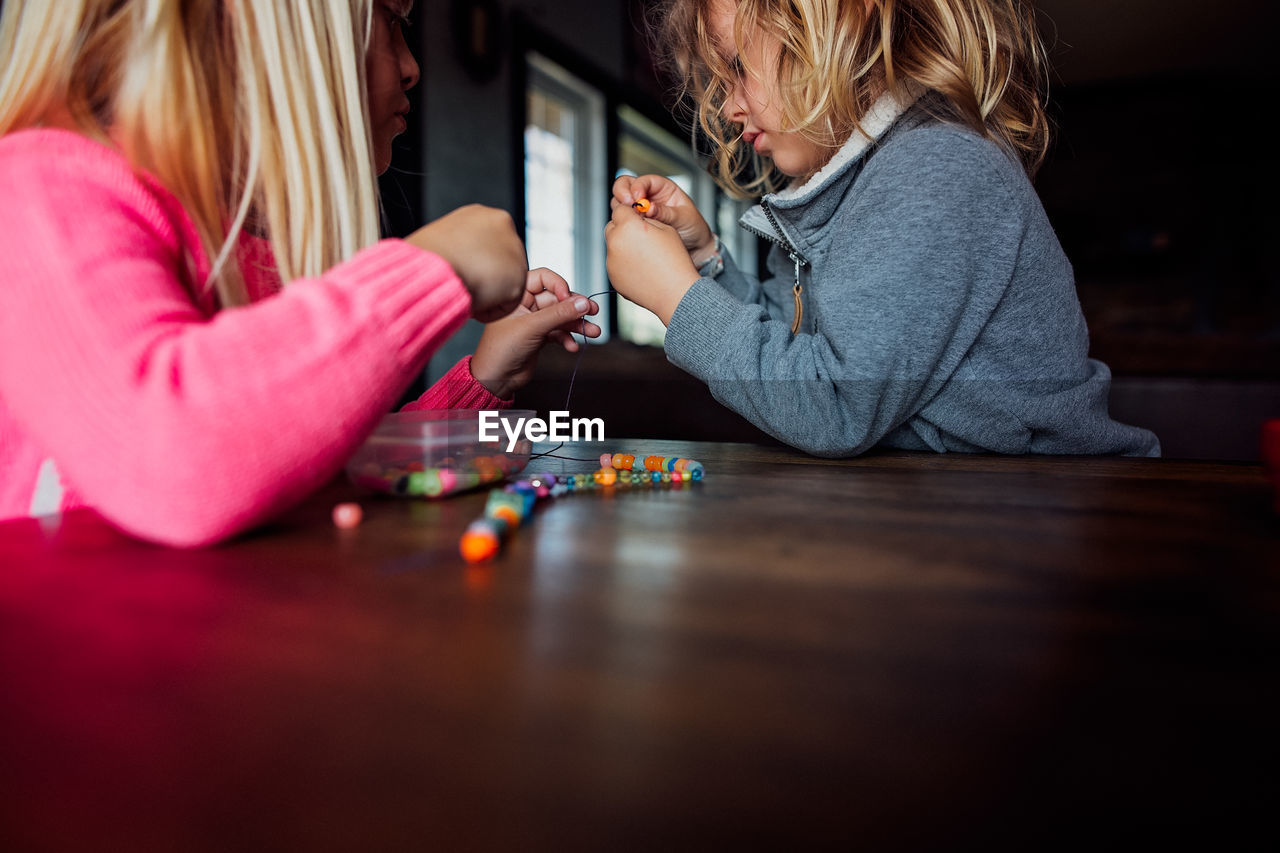 Little boy and girl making bead necklace inside at a table