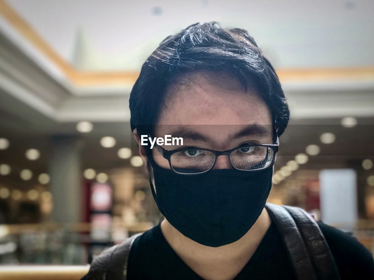 Close-up portrait of a serious young man against skylight and ceiling in shopping mall.