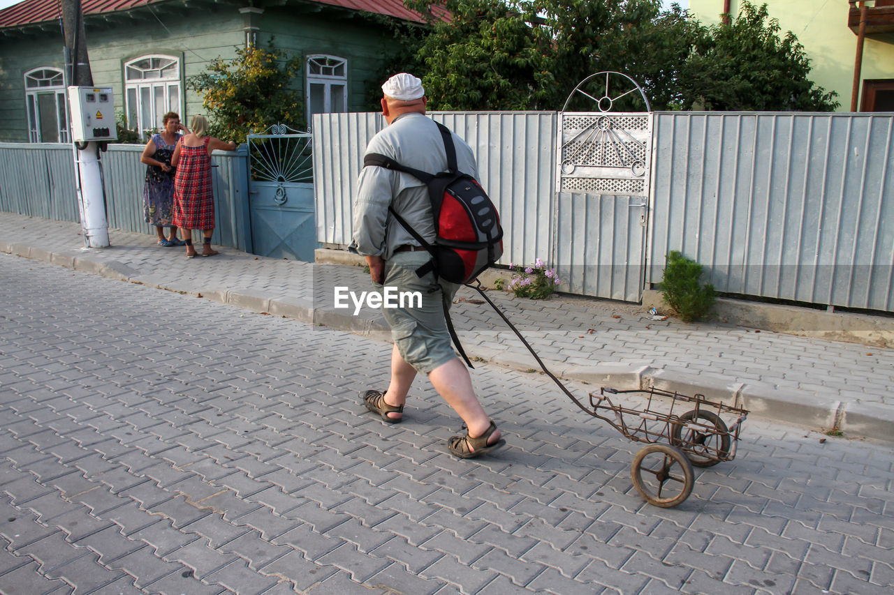 REAR VIEW OF MAN WALKING ON FOOTPATH BY BUILDING